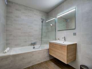 This modern bathroom features a sleek design with large, light grey tiles on the walls and a wooden vanity with a white countertop and sink.