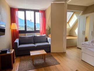 Experience breathtaking mountain views from this charming apartment, featuring a comfortable living area with a plush sofa and a modern entertainment setup.
