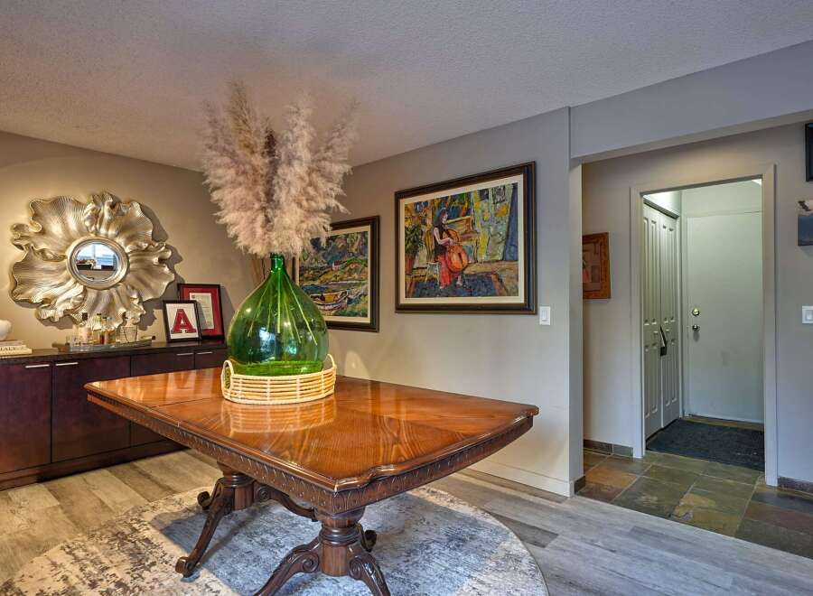 This elegant dining area features a polished wooden table adorned with a large green glass vase filled with pampas grass, creating a striking centerpiece.