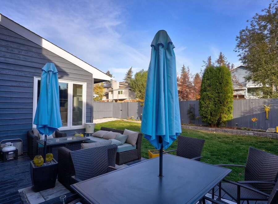 Enjoy outdoor living in this spacious backyard featuring a comfortable patio set with plush cushions and two large blue umbrellas for ample shade.