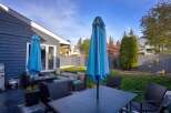 Enjoy outdoor living in this spacious backyard featuring a comfortable patio set with plush cushions and two large blue umbrellas for ample shade.