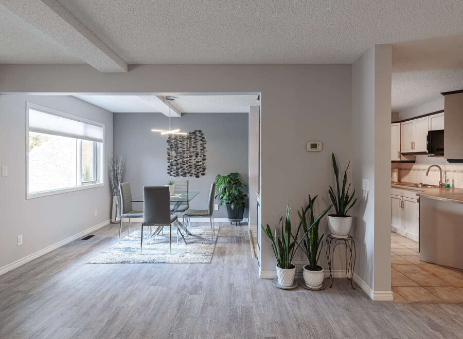 This spacious dining and living area features a modern glass-top dining table with sleek chairs, complemented by a stylish abstract wall art and a large window offering natural light.