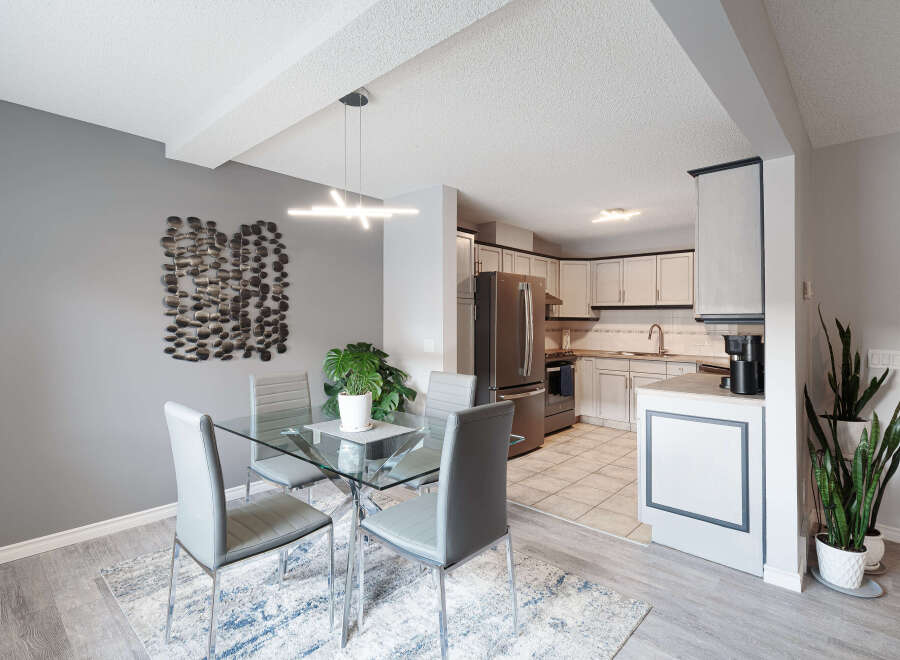This modern dining area features a sleek glass-top dining table with four grey upholstered chairs, complemented by a stylish abstract rug.