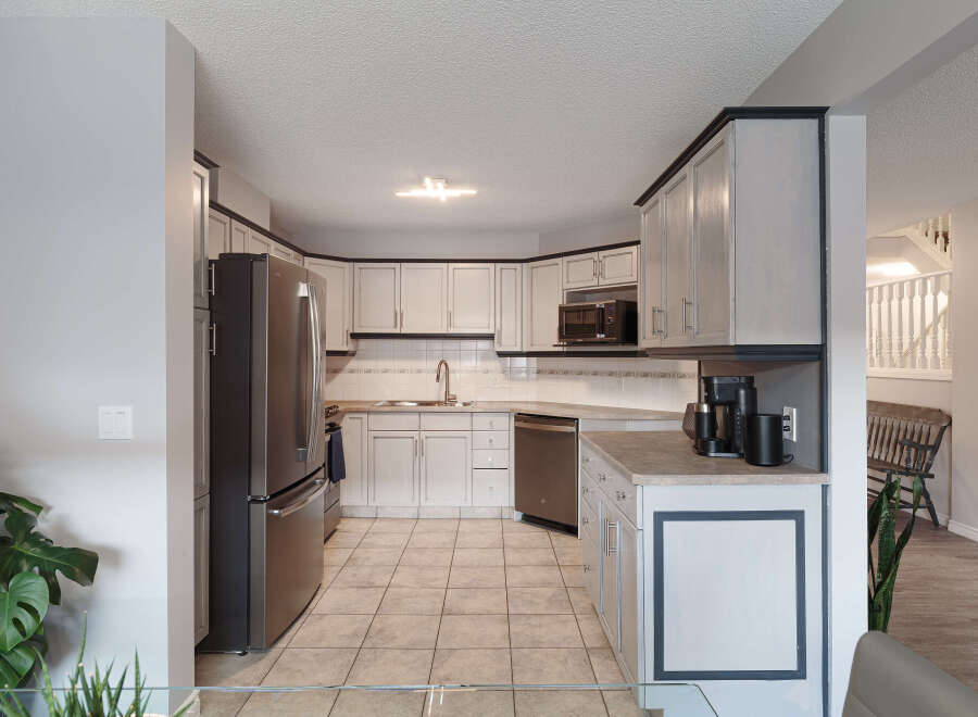 This spacious kitchen features light gray cabinetry with dark trim, complemented by a stainless steel refrigerator and dishwasher.