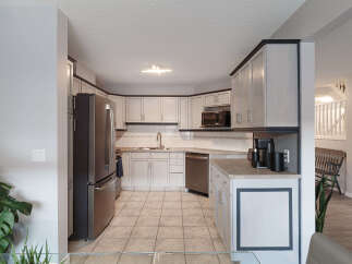 This spacious kitchen features light gray cabinetry with dark trim, complemented by a stainless steel refrigerator and dishwasher.