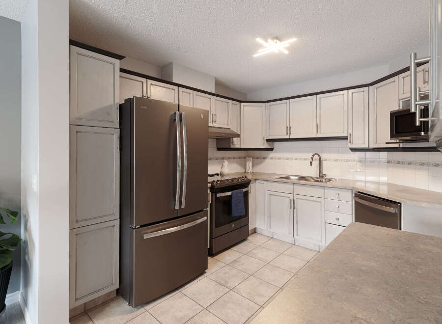 This kitchen features a sleek stainless steel refrigerator and a matching range, complemented by light-colored cabinetry with dark trim.