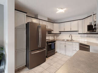 This kitchen features a sleek stainless steel refrigerator and a matching range, complemented by light-colored cabinetry with dark trim.
