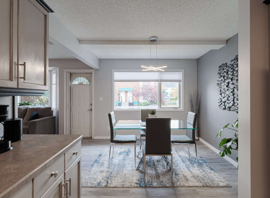This dining area features a sleek glass-top dining table with modern dark chairs, complemented by a stylish abstract rug.