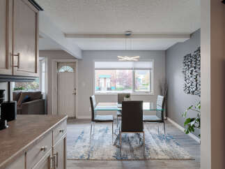 This dining area features a sleek glass-top dining table with modern dark chairs, complemented by a stylish abstract rug.