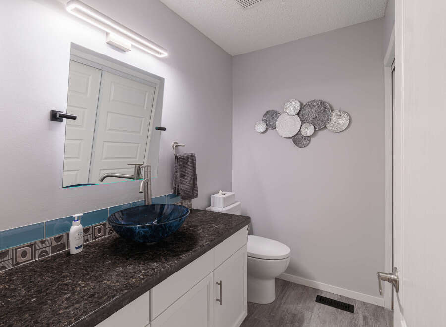 This modern bathroom features a sleek vanity with a dark granite countertop and a striking blue glass vessel sink.
