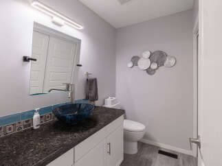 This modern bathroom features a sleek vanity with a dark granite countertop and a striking blue glass vessel sink.