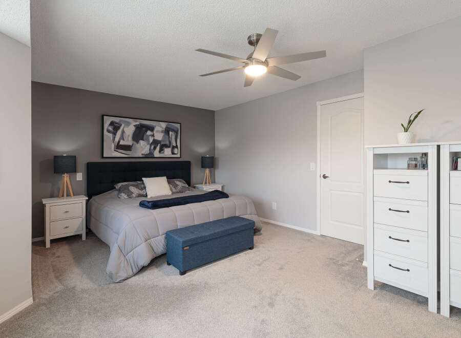 This master bedroom offers a serene retreat with its plush grey carpeting and a striking dark blue upholstered headboard.