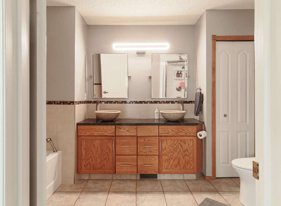 This spacious bathroom features a double vanity with vessel sinks and granite countertops, complemented by ample wooden cabinetry for storage.