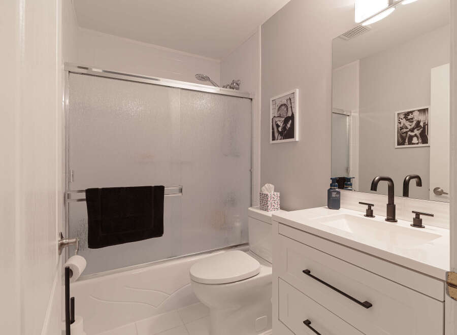 This modern bathroom features a sleek white vanity with black hardware, complemented by a white countertop and a matching sink.