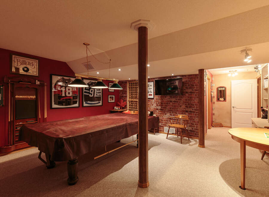 This basement game room is perfect for entertaining, featuring a large pool table covered with a protective brown cloth.