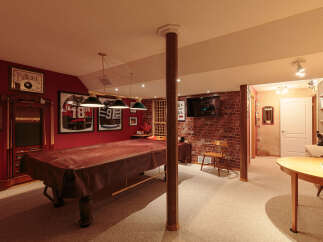This basement game room is perfect for entertaining, featuring a large pool table covered with a protective brown cloth.