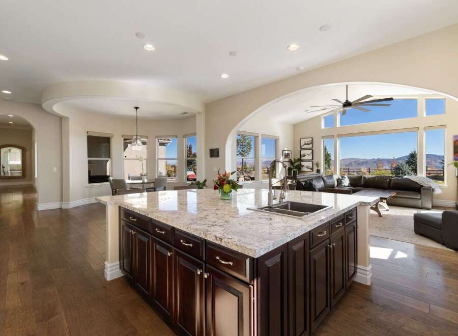 Experience breathtaking panoramic views from this stunning kitchen, featuring a large granite island with a double sink and ample dark wood cabinetry.
