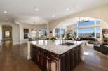 Experience breathtaking panoramic views from this stunning kitchen, featuring a large granite island with a double sink and ample dark wood cabinetry.