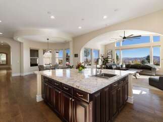 Experience breathtaking panoramic views from this stunning kitchen, featuring a large granite island with a double sink and ample dark wood cabinetry.