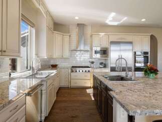 This spacious kitchen boasts elegant cream-colored cabinetry with detailed trim, complemented by stunning granite countertops.