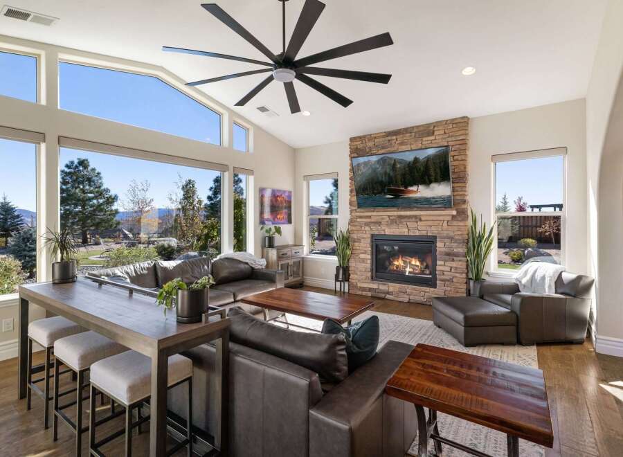 Experience breathtaking mountain views from this stunning living room, featuring a massive stone fireplace and a large, multi-pane window wall.