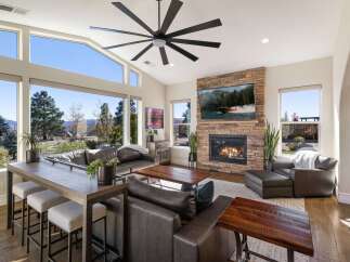 Experience breathtaking mountain views from this stunning living room, featuring a massive stone fireplace and a large, multi-pane window wall.