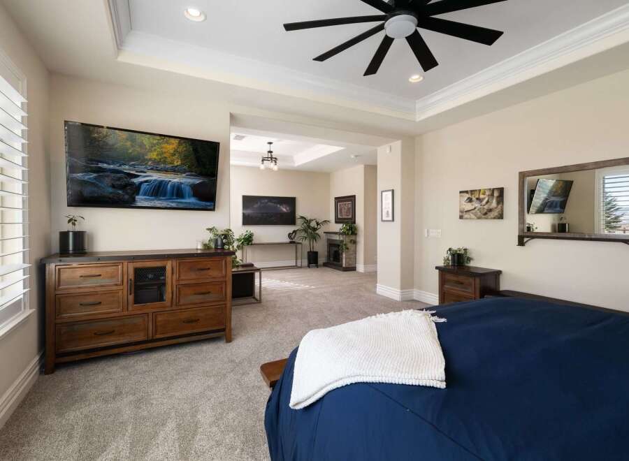 Experience luxury and comfort in this beautifully appointed bedroom, featuring a large wall-mounted TV, a rustic wooden dresser, and a plush navy blue bed with a cozy white throw.