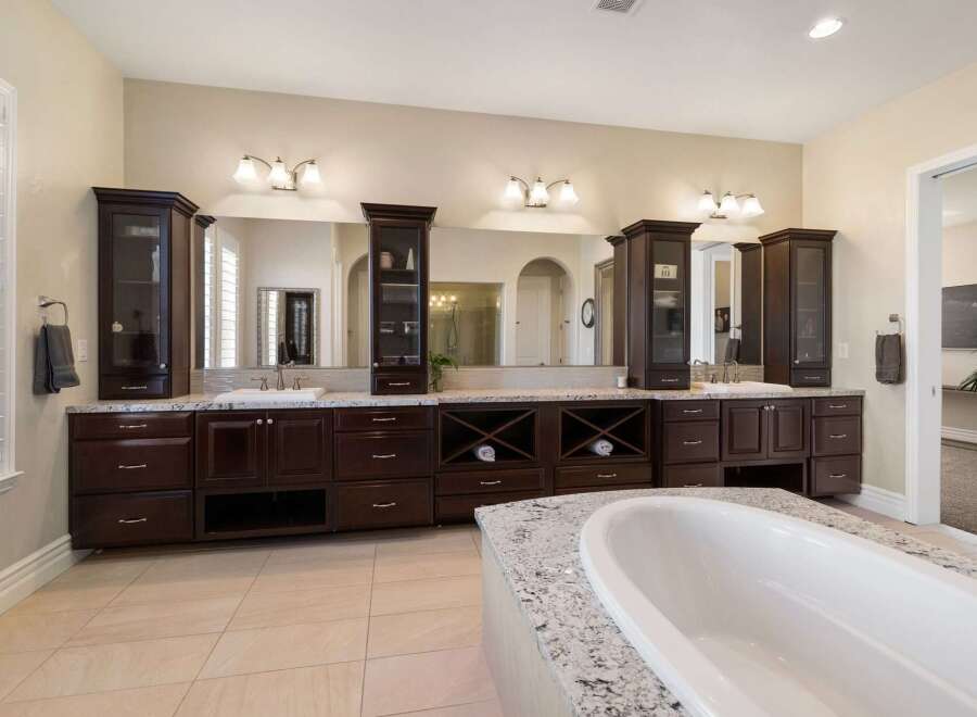 Indulge in luxury with this stunning master bathroom, featuring a spacious double vanity with dark wood cabinetry and granite countertops.