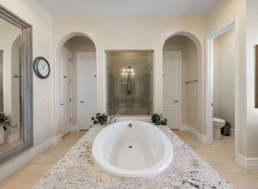 Indulge in luxury in this stunning master bathroom, featuring a freestanding soaking tub set atop a granite vanity.