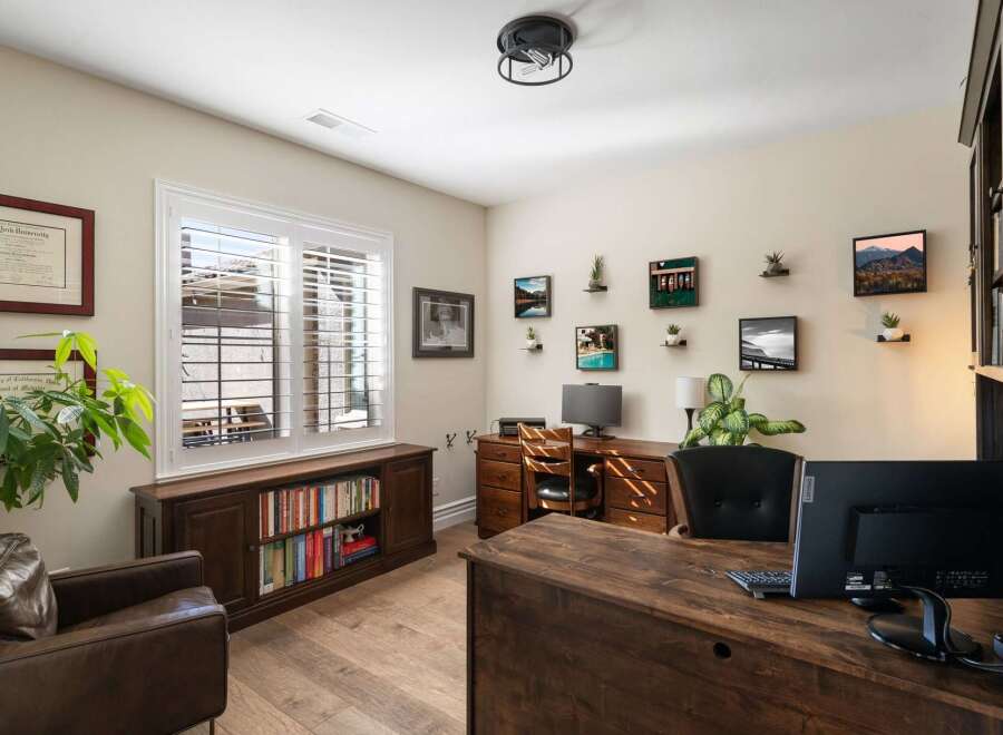 This home office features a spacious wooden desk with dual monitors, complemented by a comfortable leather armchair and a built-in bookshelf filled with literature.