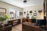 This home office features a spacious wooden desk with dual monitors, complemented by a comfortable leather armchair and a built-in bookshelf filled with literature.