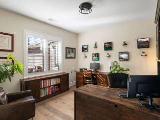 This home office features a spacious wooden desk with dual monitors, complemented by a comfortable leather armchair and a built-in bookshelf filled with literature.