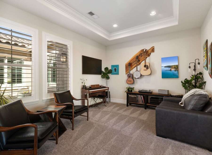 This inviting living room features a stylish entertainment setup with a piano, a television, and a collection of musical instruments displayed on the wall.