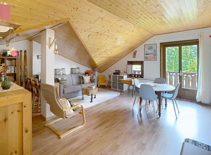 Experience cozy living in this charming attic apartment, featuring a warm wooden ceiling and a comfortable living area with a grey sofa and accent pillows.