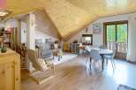 Experience cozy living in this charming attic apartment, featuring a warm wooden ceiling and a comfortable living area with a grey sofa and accent pillows.