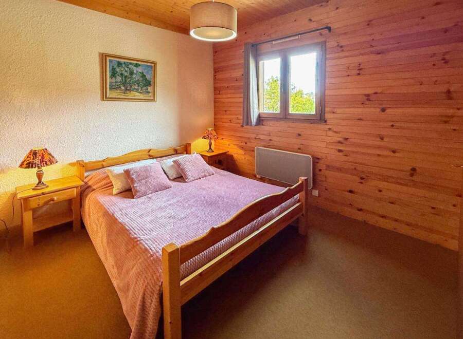 Experience cozy comfort in this charming bedroom, featuring a warm wooden interior and a comfortable bed adorned with pink linens.