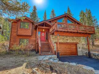Experience mountain living in this stunning wooden home, featuring a welcoming red front door and a spacious wooden deck perfect for enjoying the crisp, clear air.