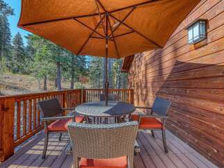 Enjoy the outdoors on this charming wooden deck, complete with a round dining table and four chairs, all shaded by a large orange umbrella.
