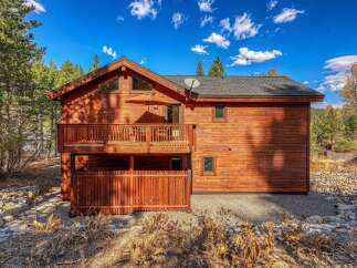 Experience rustic charm in this stunning wooden home, nestled amidst tall pine trees under a vibrant blue sky.