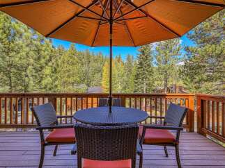 Enjoy outdoor dining with this charming patio set, featuring a round table and four wicker chairs with orange cushions, all shaded by a large orange umbrella.