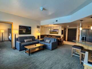 This spacious living area features comfortable blue sofas, a wooden coffee table, and a dining area with a long bench and chairs.
