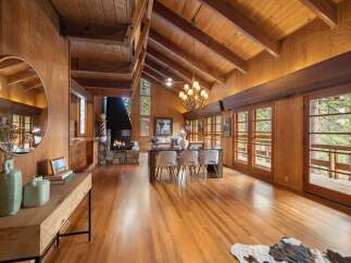 Experience rustic charm in this spacious living and dining area, featuring a grand stone fireplace and a vaulted wood-beamed ceiling.
