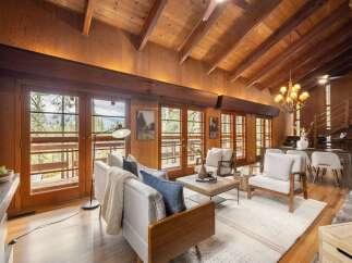 Experience rustic charm in this spacious living room, featuring a vaulted wood-beamed ceiling and abundant natural light streaming through large glass doors.