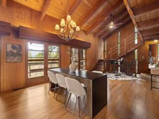 Experience rustic charm in this spacious dining and living area, featuring a vaulted wood-paneled ceiling with exposed beams and a grand chandelier.