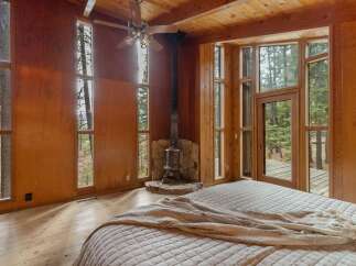 Experience rustic charm in this bedroom featuring a cozy wood-burning stove and expansive windows that bring the outdoors in.