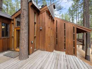 Nestled among tall pines, this unique home features a striking wooden exterior and a spacious deck perfect for enjoying the natural surroundings.