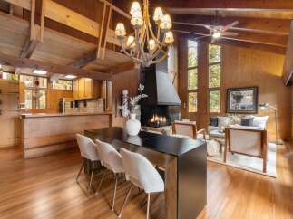 Experience rustic charm in this spacious living and dining area, featuring a grand stone fireplace and a vaulted wood-paneled ceiling with exposed beams.