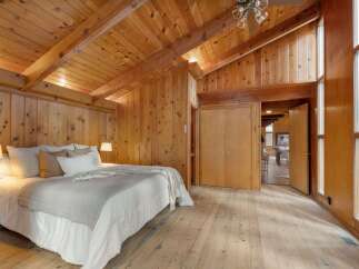 Experience rustic charm in this beautifully appointed bedroom, featuring warm wood paneling throughout the walls and vaulted ceilings with exposed beams.
