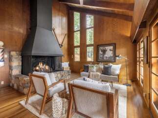 Experience rustic charm in this cozy living room, featuring a grand stone fireplace with a modern black hood, perfect for warming up on chilly evenings.
