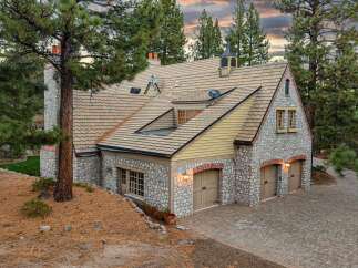 This charming stone-clad garage boasts a rustic architectural style, featuring a multi-level roof with tan shingles and a cupola.